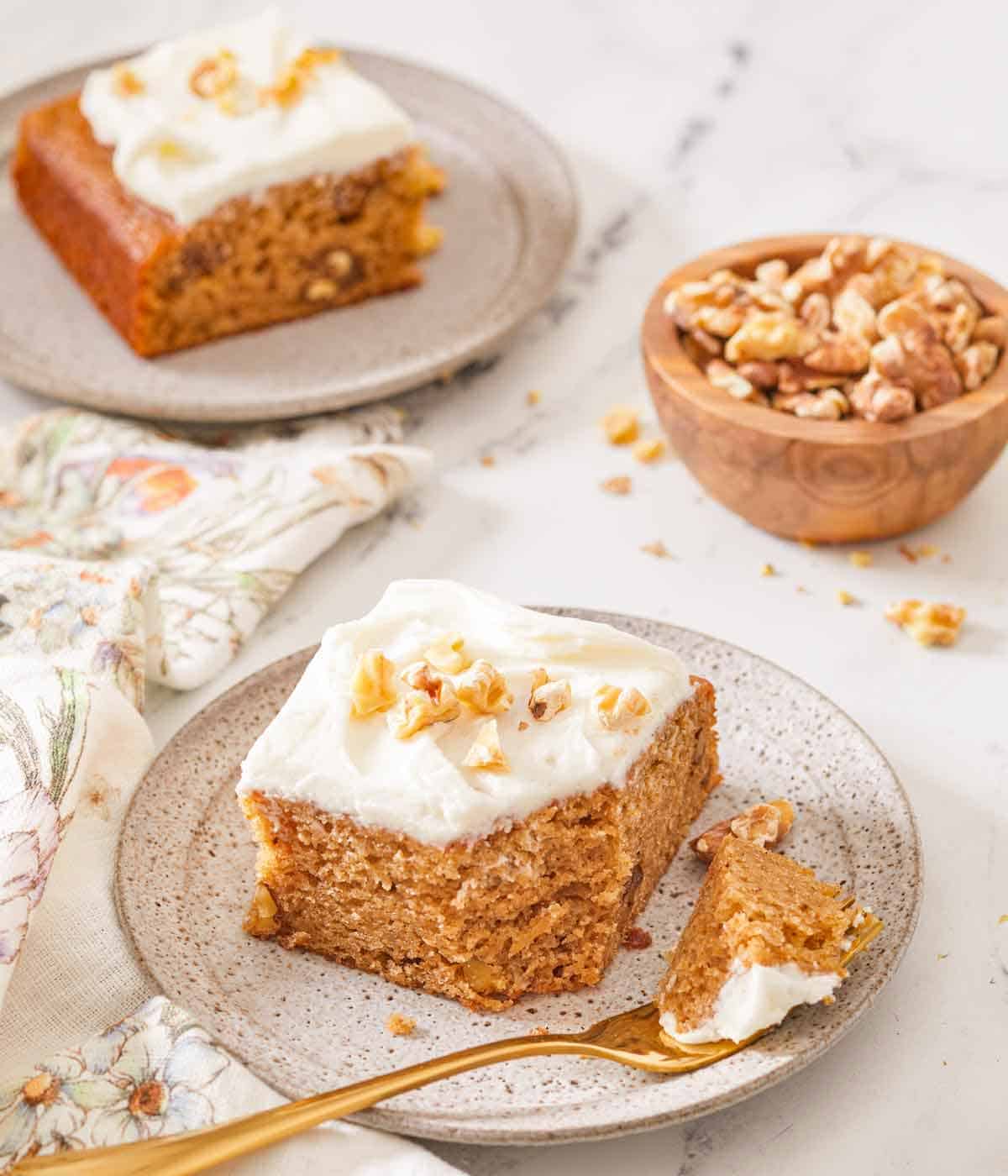 Two plates each with a square piece of applesauce cake with the one in front with a bite taken off on a fork.