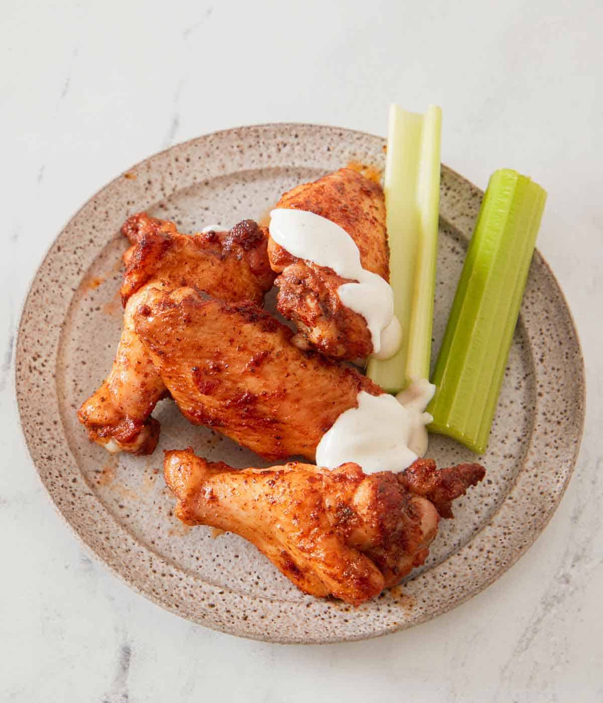 A plate with chicken wings and celery with sauce drizzled over a couple.