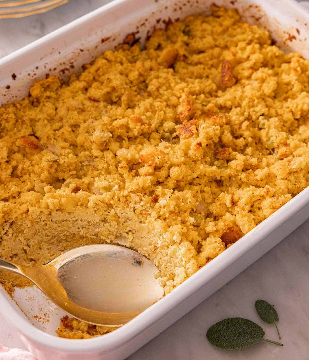 A baking dish with cornbread dressing with a spoon in the corner where some got scooped out.
