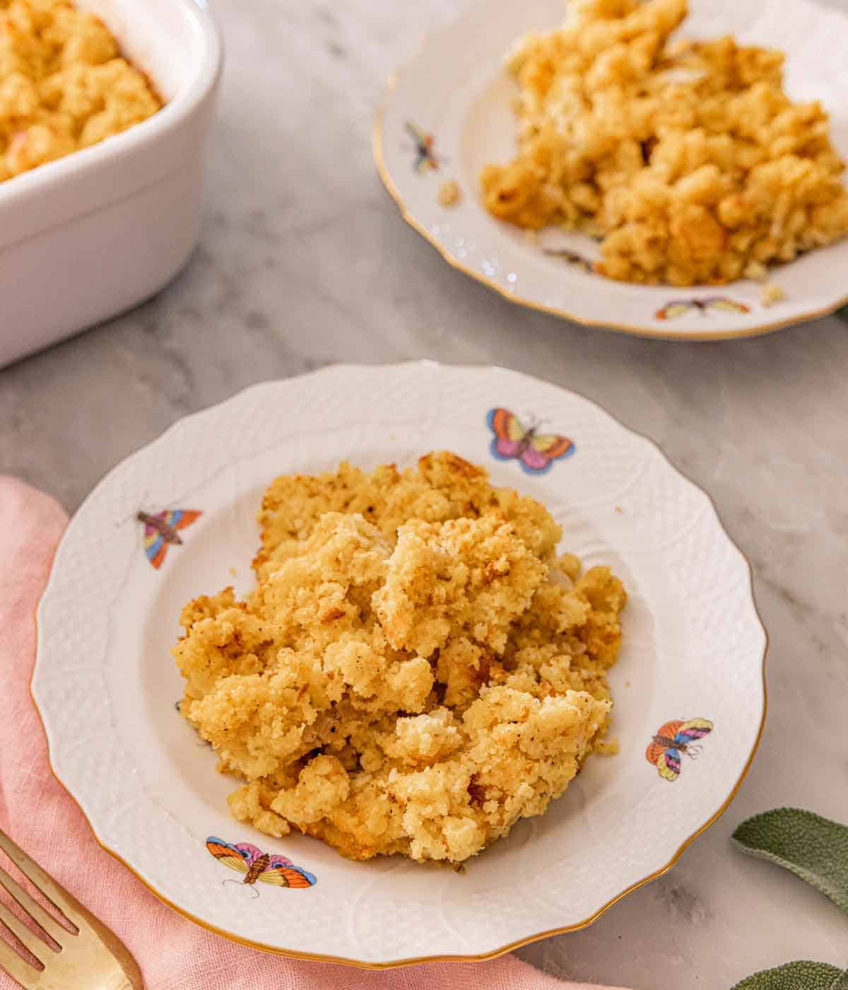 A plate with cornbread dressing with another plateful and baking dish in the background.