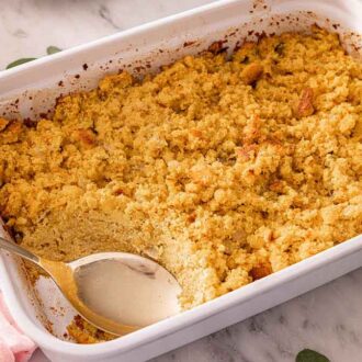 A white baking dish with cornbread dressing with a serving spoon in the corner of the dish.