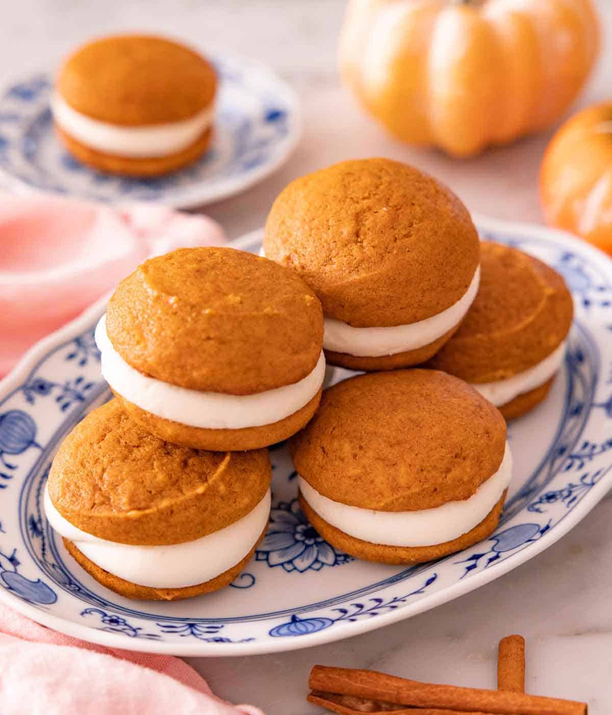 A platter with a stack of pumpkin whoopie pies with pumpkins in the background.