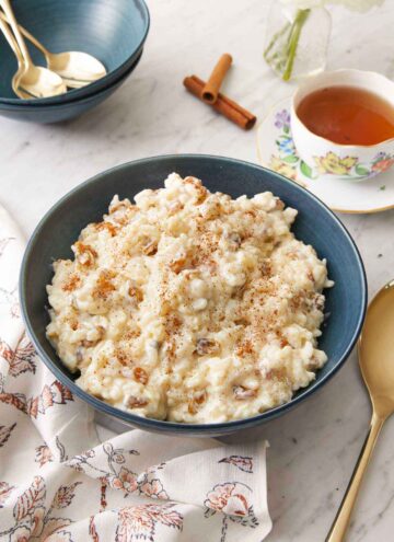 A blue bowl of rice pudding with a cup of tea in the background.