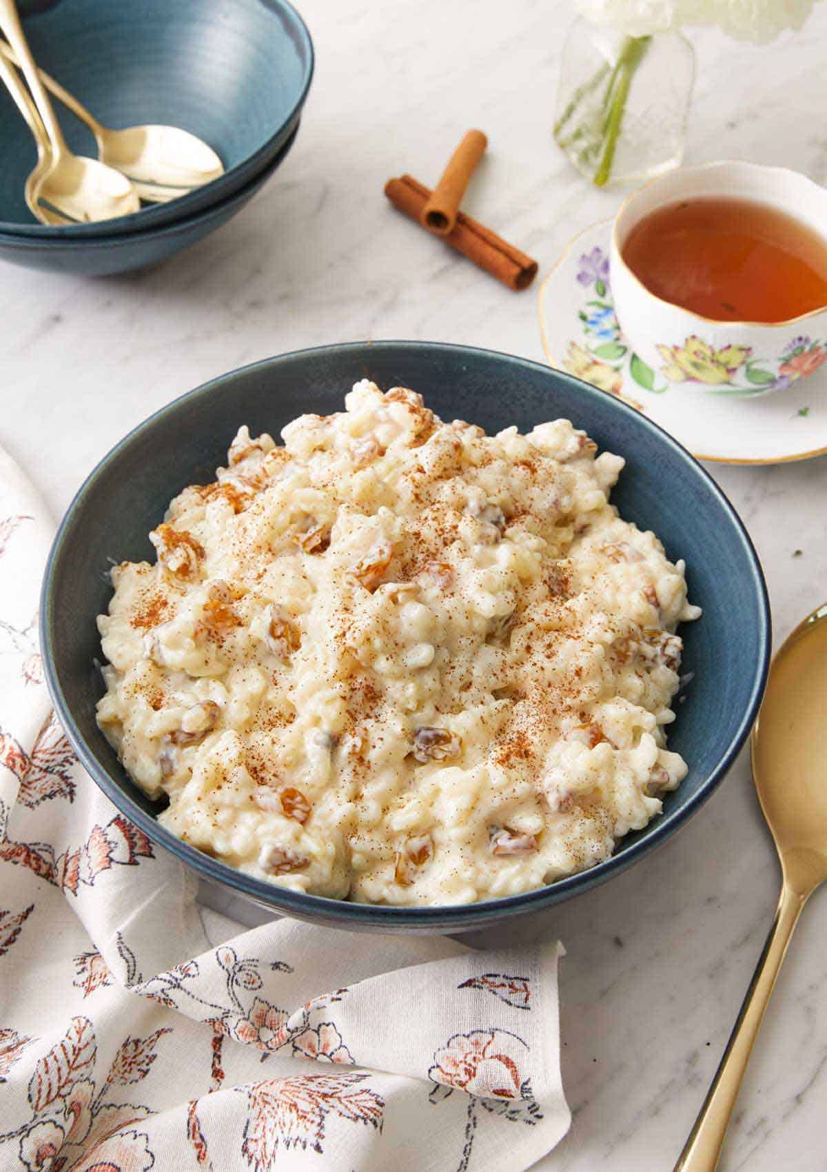 A blue bowl of rice pudding with a cup of tea in the background.