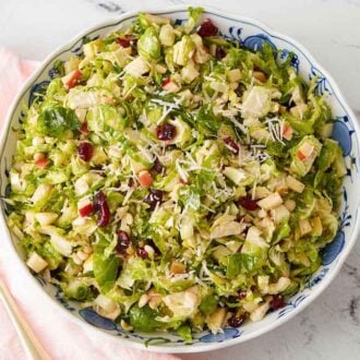 A bowl of Brussels sprout salad with shaved cheese on top with a linen and spoon beside the bowl.