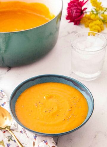 A bowl of butternut squash soup with a glass of water and pot of soup off to the side.