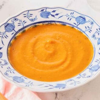 A blue and white bowl of butternut squash soup with a spoon on the side.