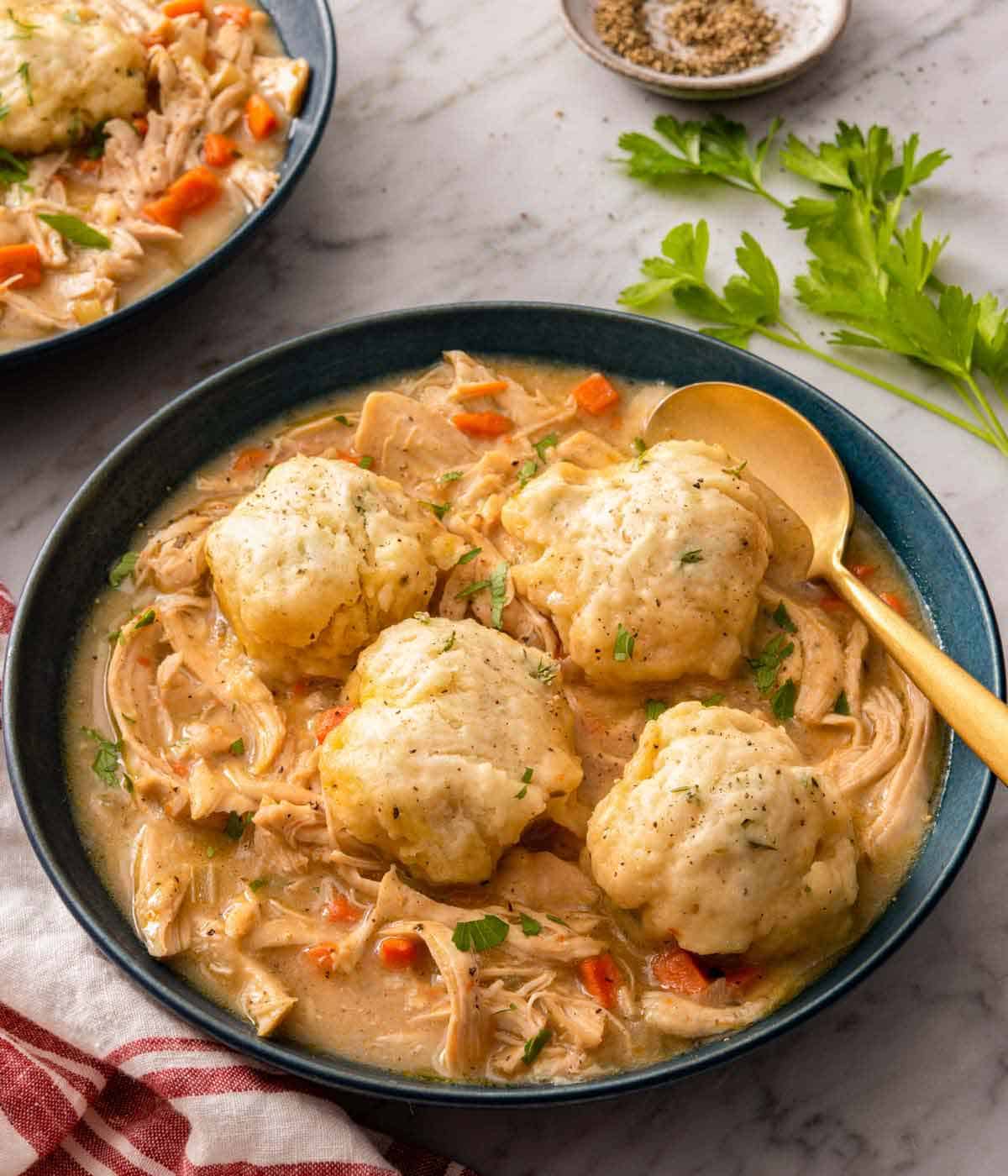 A blue bowl of chicken and dumplings with a spoon tucked in and fresh cilantro on the side.