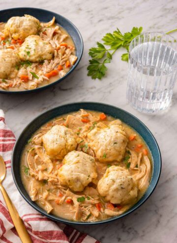 Two bowls of chicken and dumplings with one in front, with a glass of water on the side.