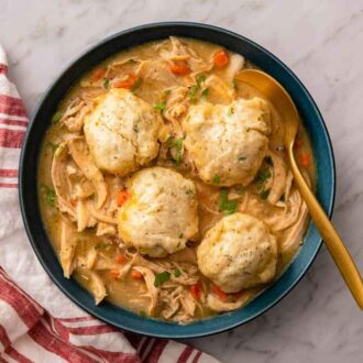 Overhead view of a bowl of chicken and dumplings with a spoon inside the bowl and a linen on the side.