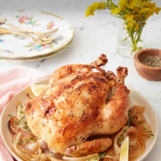 Pinterest graphic of a roasted chicken over a plate of onions and lemon with flowers in the background.