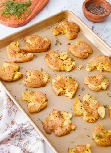 A sheet pan with multiple smashed potatoes with fresh dill and pepper on the side.