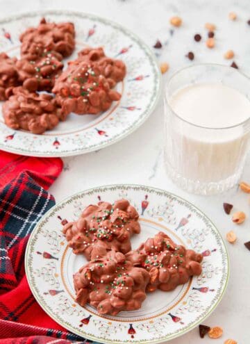 A plate with three clusters of crockpot candy with a milk behind it and another plate of candies.