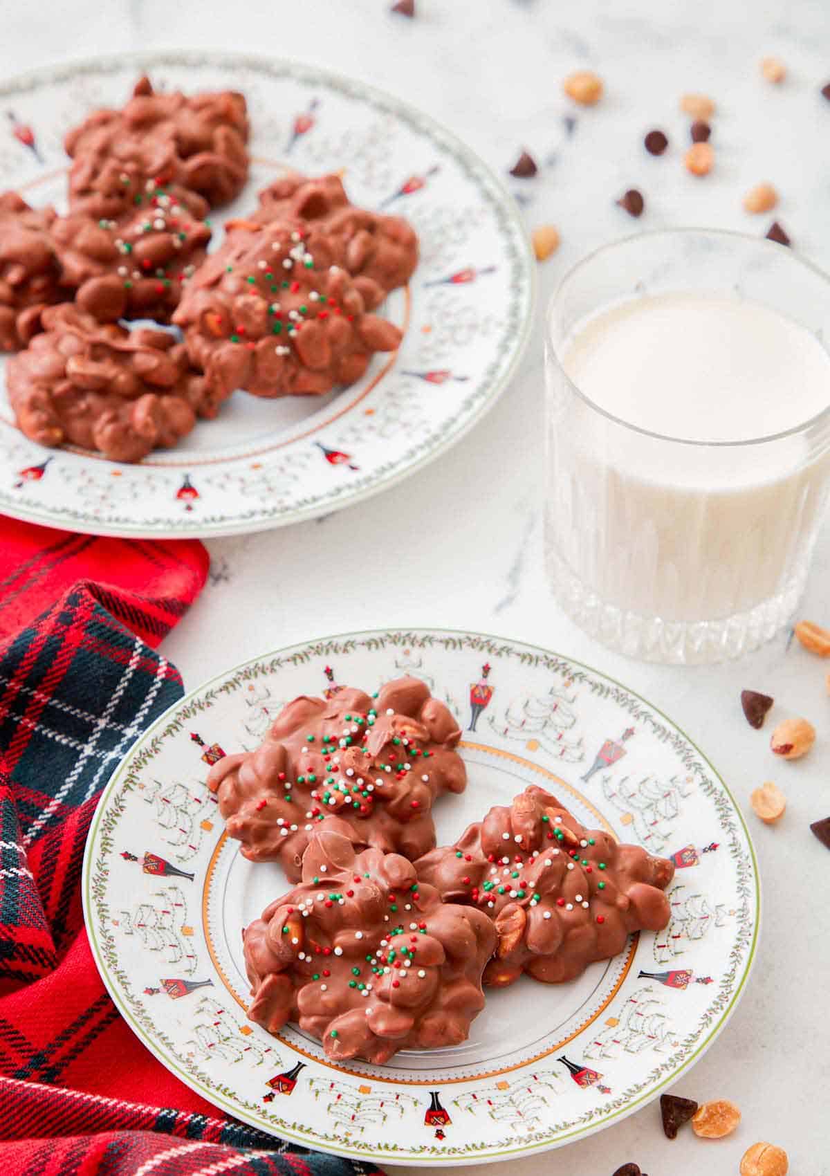 A plate with three clusters of crockpot candy with a milk behind it and another plate of candies.