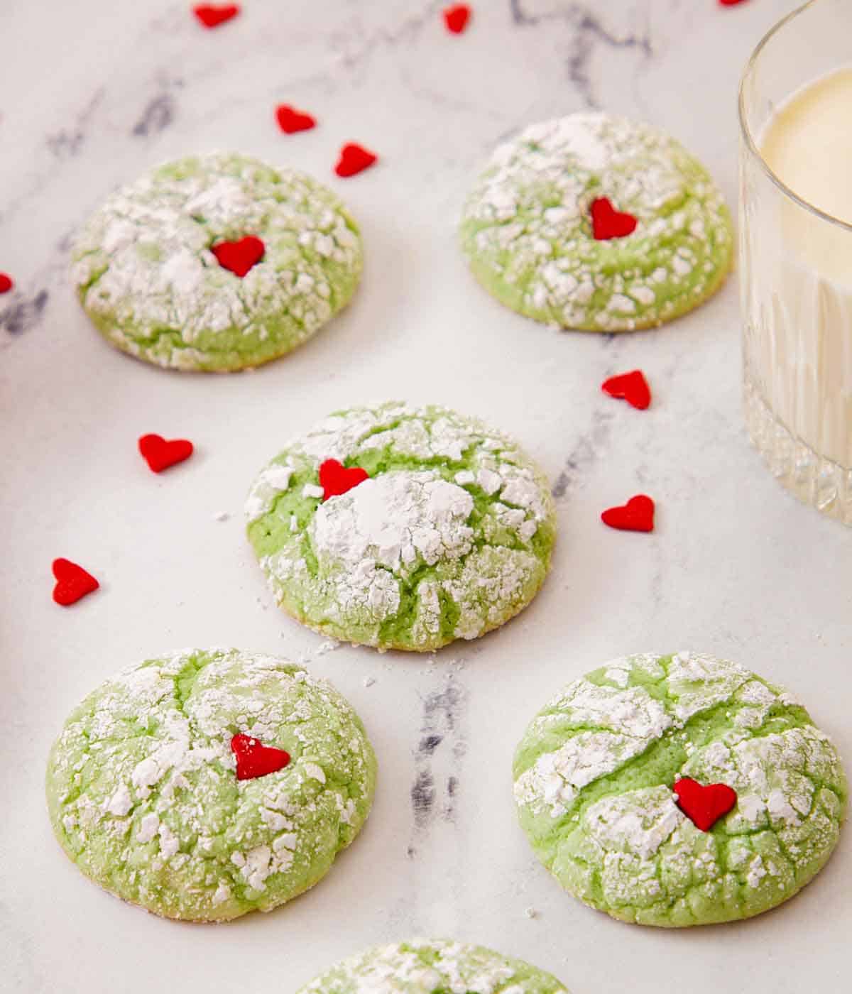 Five Grinch cookies with heart sprinkles scattered around.