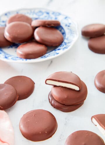 Multiple peppermint patties scattered with the focus on a stack of three in the middle, the top one cut in half.