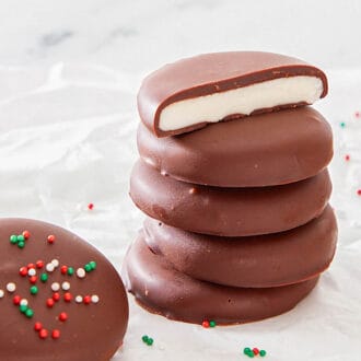 A stack of peppermint patties with the top one cut in half, surrounded by more peppermint patties with sprinkles on top.