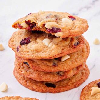 A stack of white chocolate cranberry cookies with a bite taken out of the top cookie.