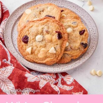 Pinterest graphic of a plate with a couple of white chocolate cranberry cookies with some white chocolate chips scattered around it.