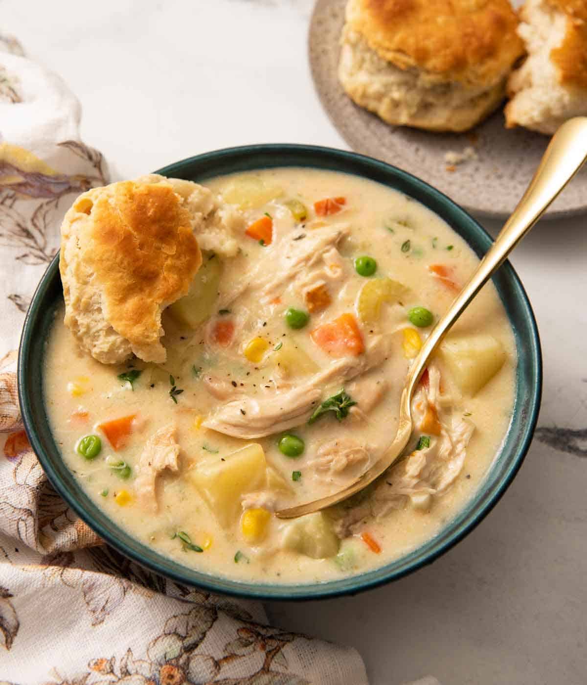 A bowl of chicken pot pie soup with a spoon and biscuit tucked into the bowl.