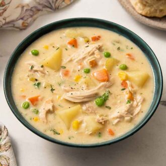 A bowl of chicken pot pie soup with a gold colored spoon beside it.