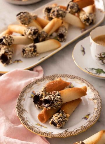 A plate with multiple chocolate dipped tuiles with a platter in the background with additional cookies.