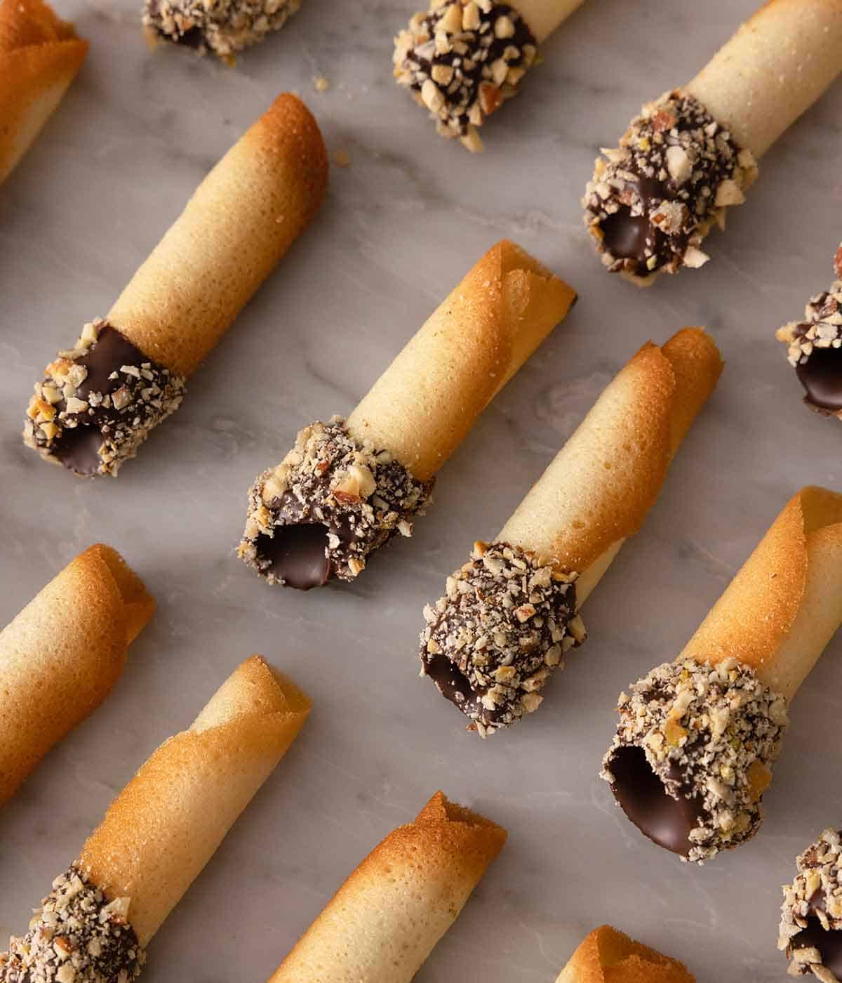Multiple chocolate dipped tuiles in three rows on a marble counter.