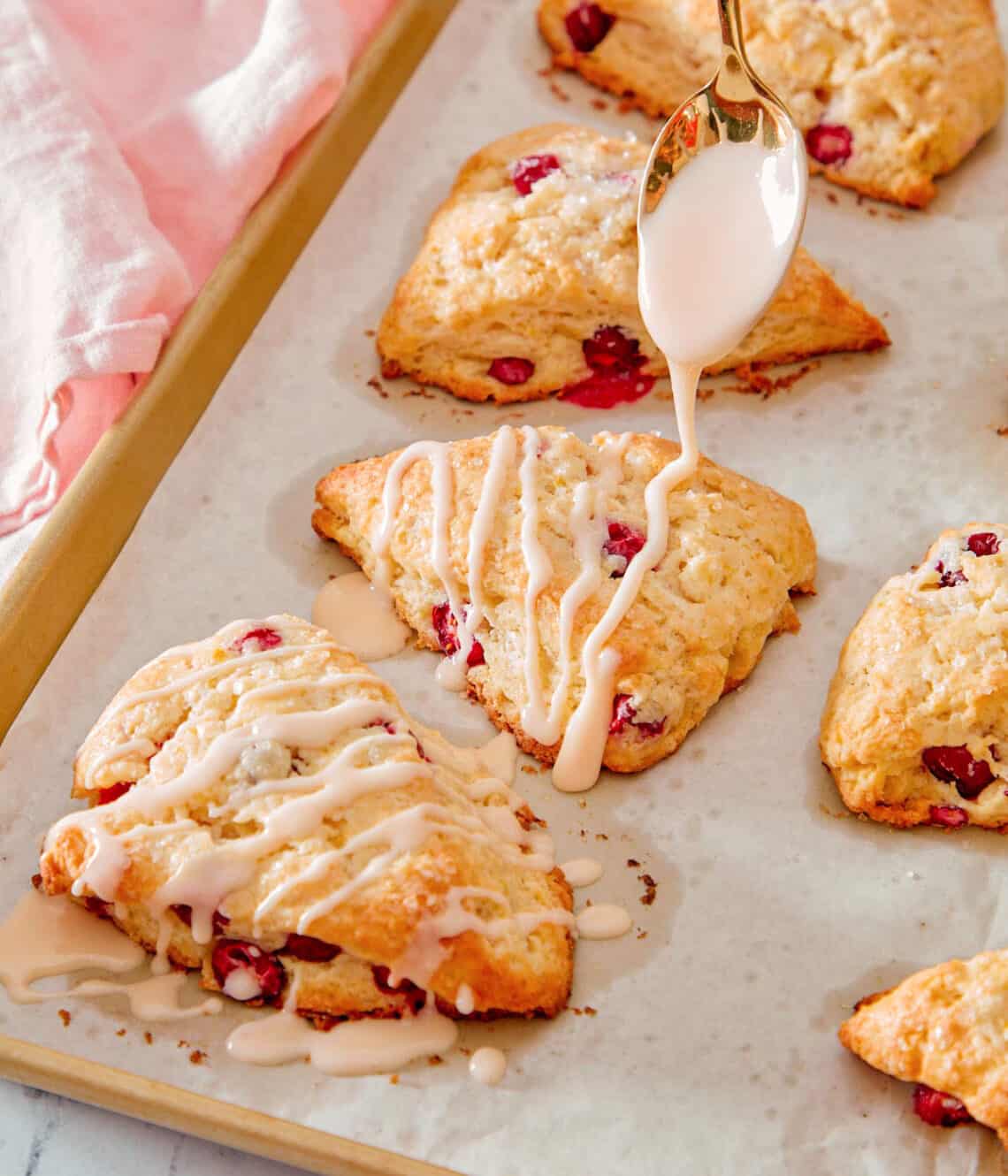Icing getting drizzled onto orange cranberry scones.
