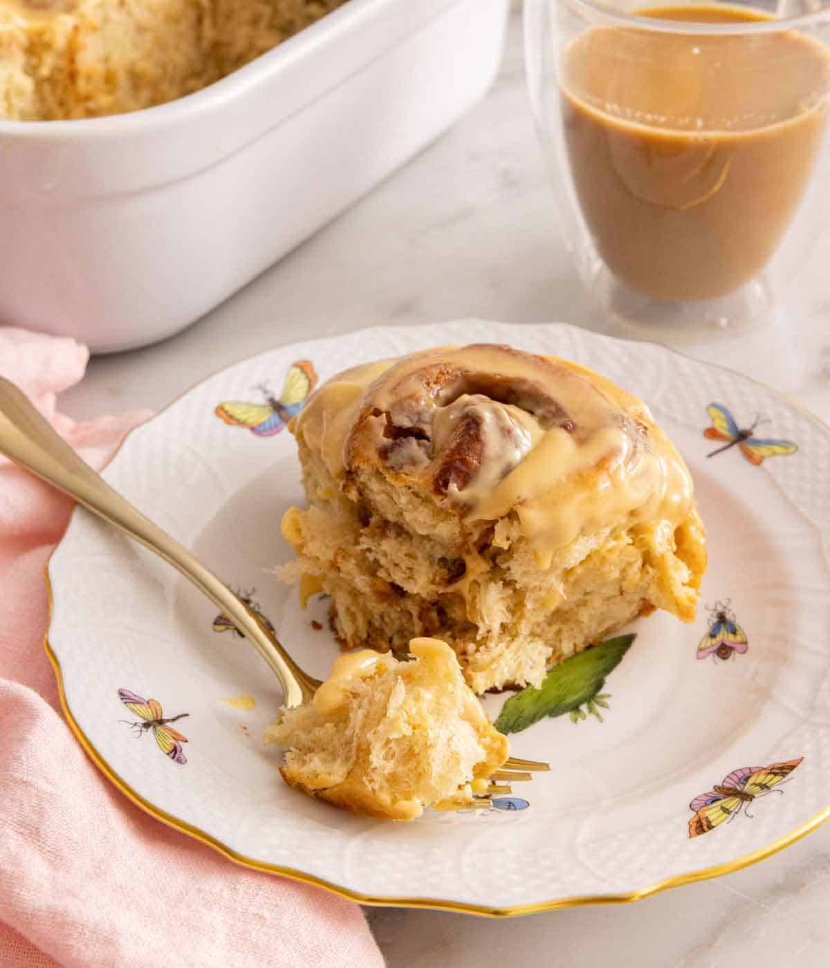 A plate with a piece of dulce de leche cinnamon roll with a bite on a fork in front.