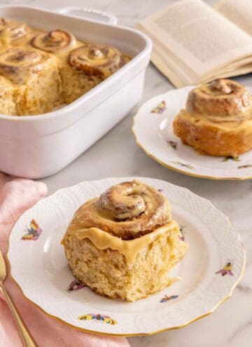 A plate with a piece of dulce de leche cinnamon roll with another in the background and the rest in a baking dish.