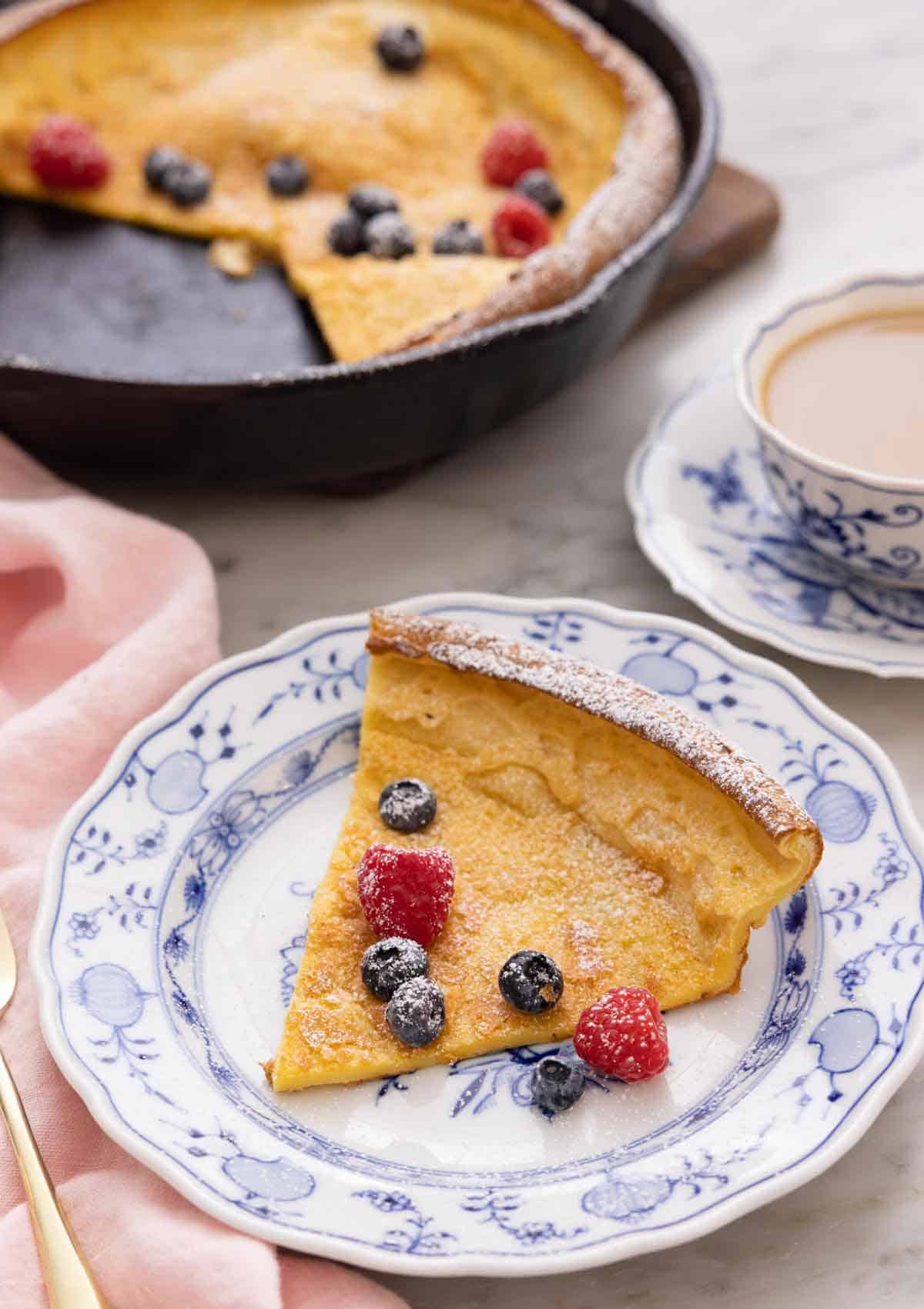 A plate with a slice of Dutch baby with fresh fruit and powdered sugar on top.