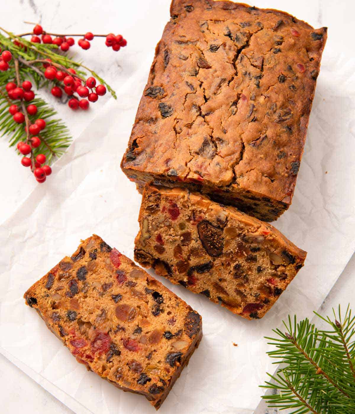 Overhead view of a loaf of fruit cake on top of parchment with two slices cut.