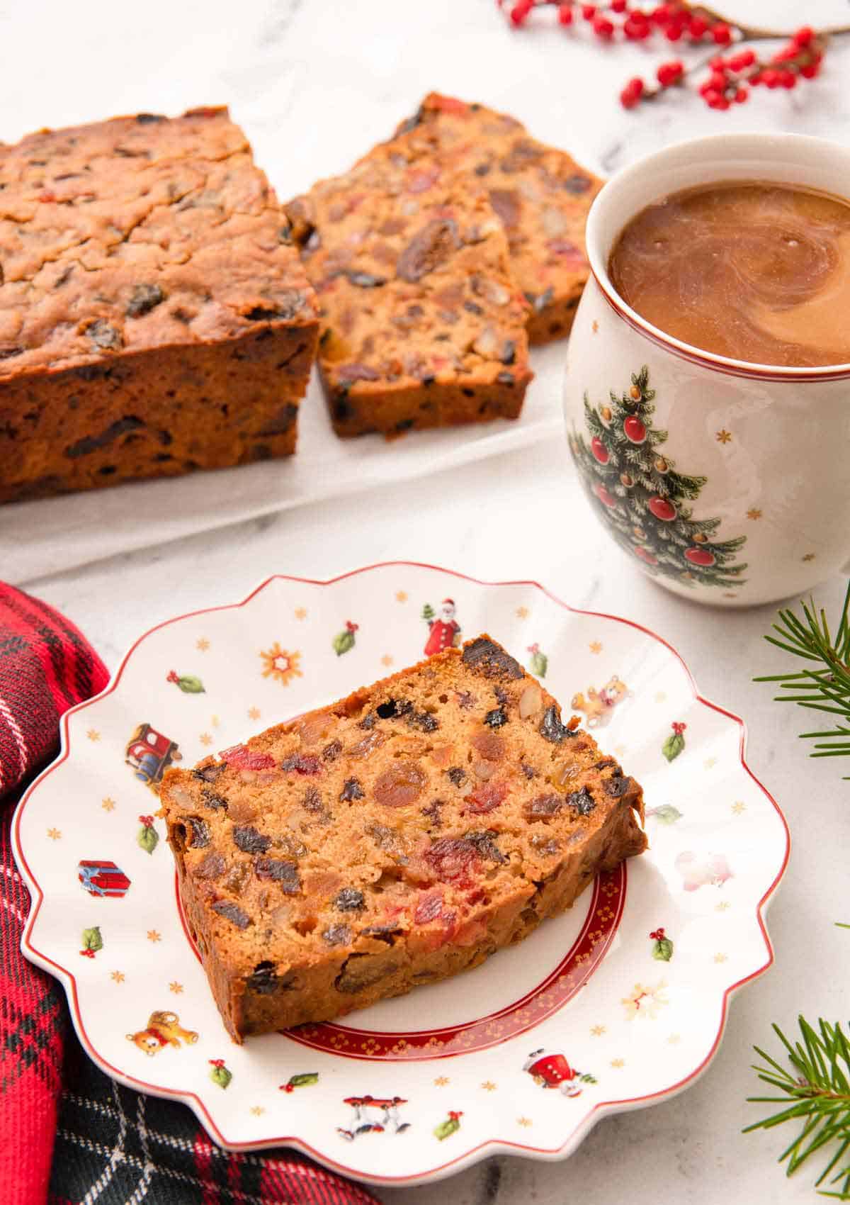 A festive plate with a slice of fruit cake with a mug of coffee and more cake behind it.