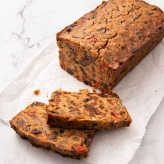 An angled view of a loaf of fruit cake with two slices cut in front of it.