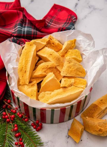 A holiday cookie tin lined with paper filled with pieces of honeycomb.