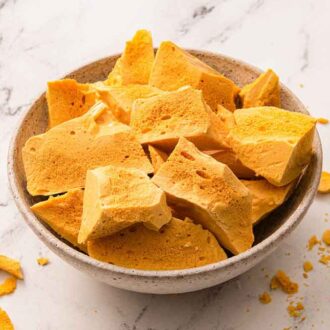 A bowl of pieces of honeycomb candy with a few crumbs scattered around.