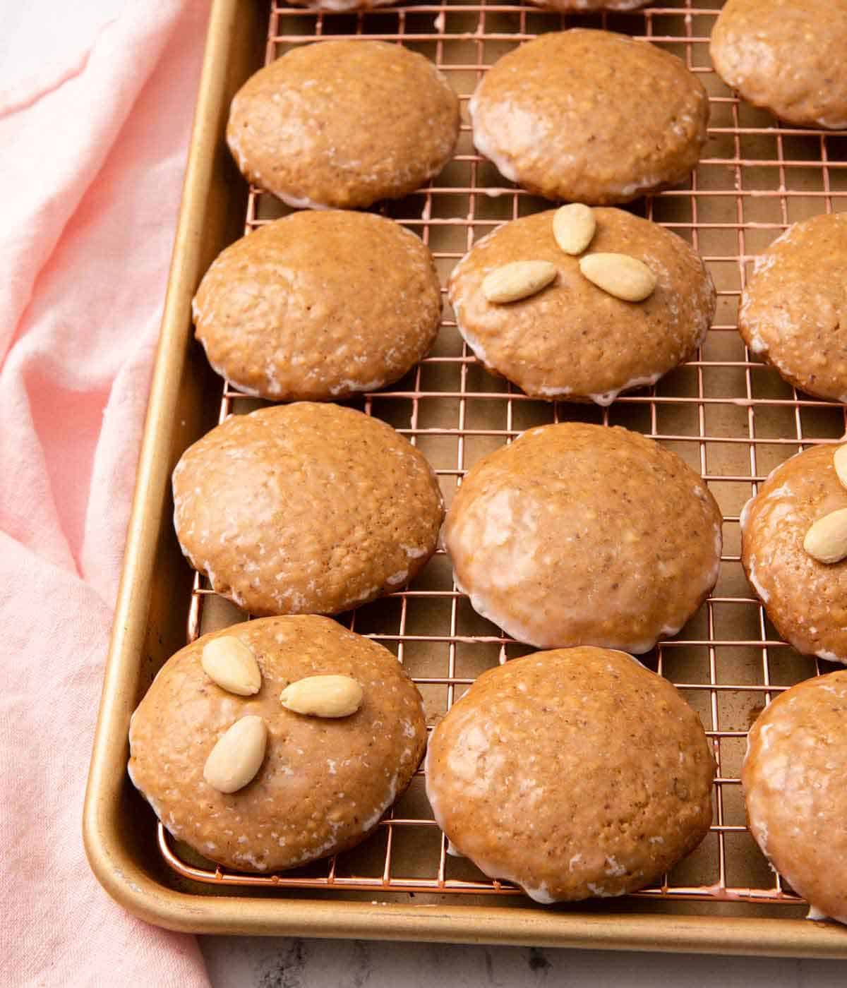 Multiple Lebkuchen on a wire rack over a sheet pan with a couple of them with three almonds on top.