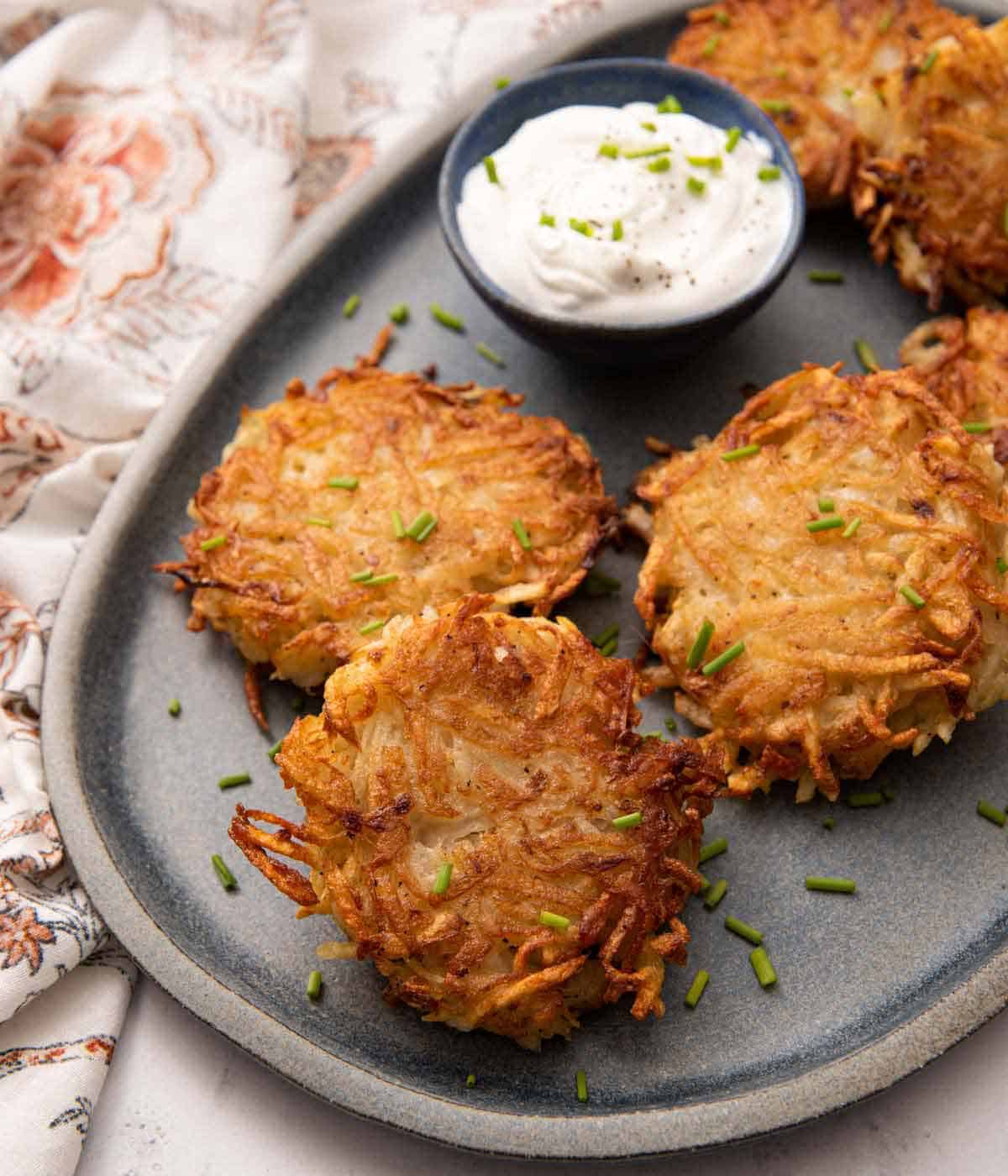 Overhead view of a grey platter with multiple potato pancakes with a small bowl of dip.