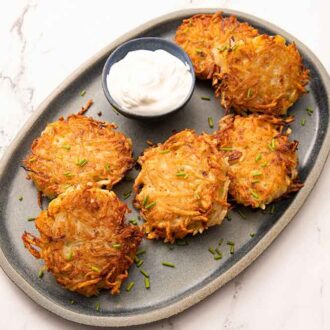 Overhead view of a grey platter with multiple potato pancakes with a small bowl of sour cream.