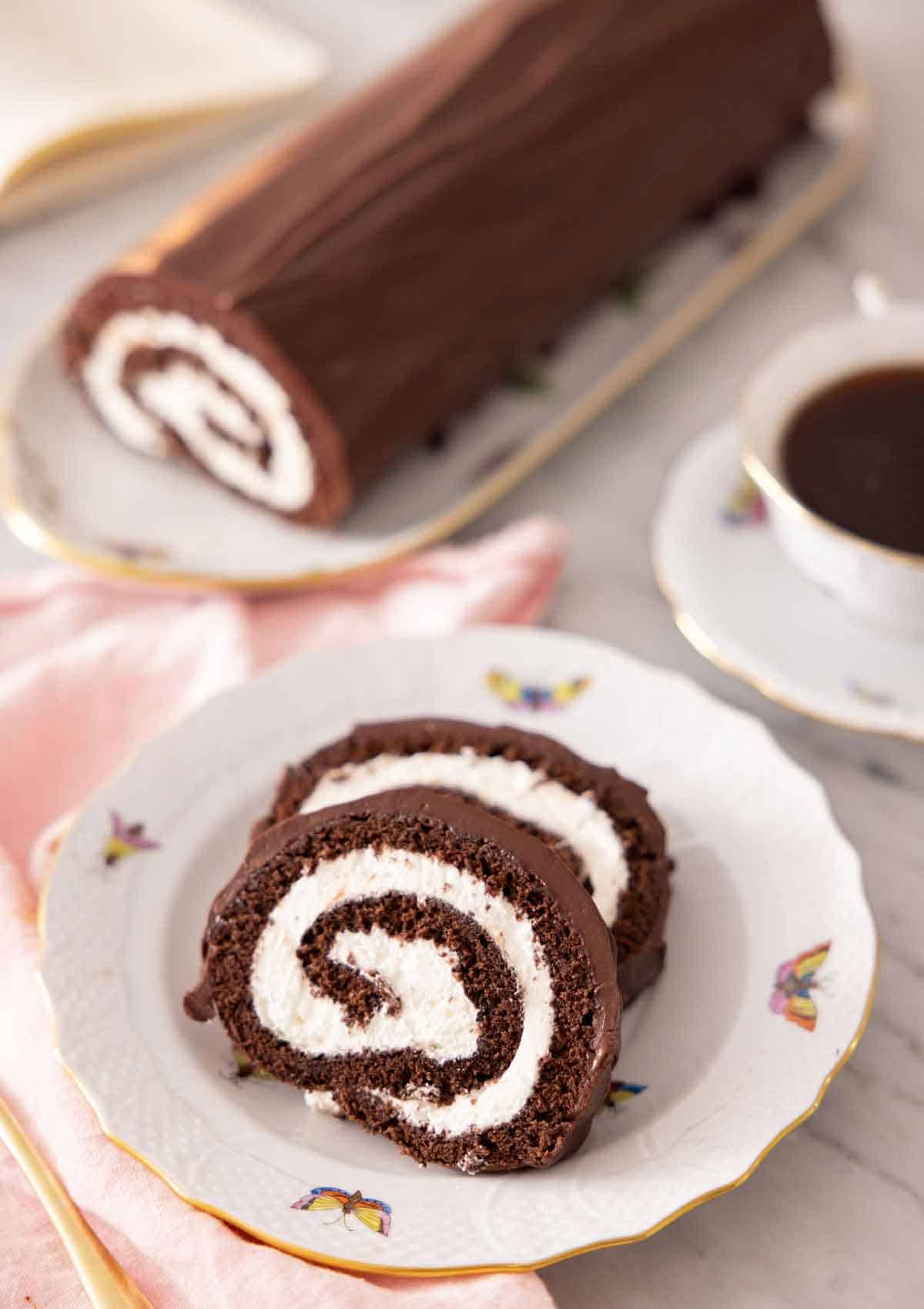 A plate with two slices of Swiss roll with the rest of the log in the background.
