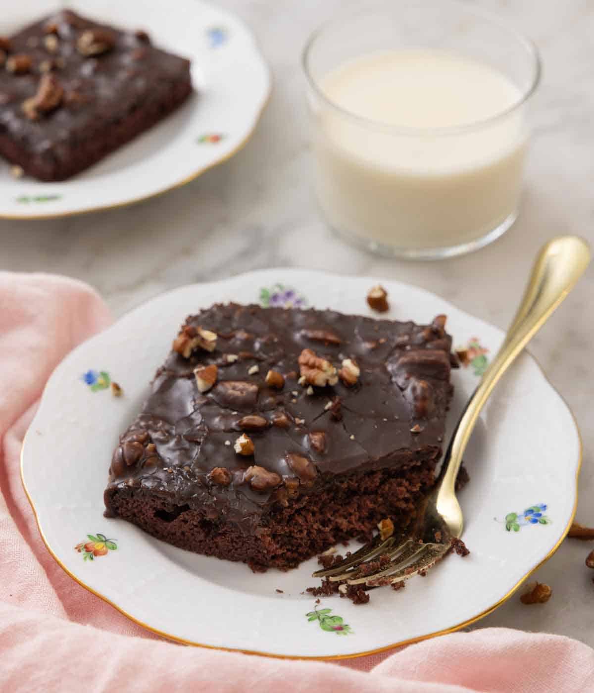 A plate with a square piece of Texas sheet cake with a corner eaten with a fork beside it.