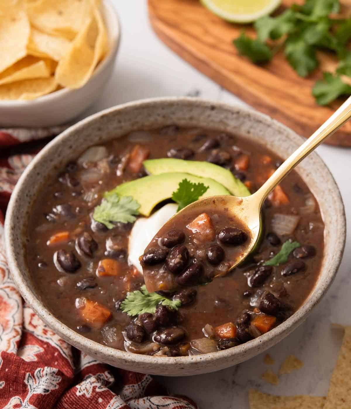 A bowl of black bean soup with a spoonful lifted up.