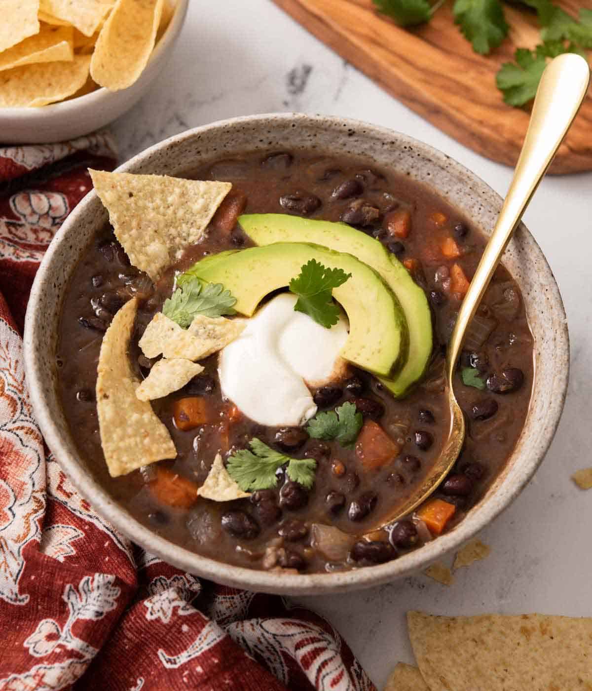A bowl of black bean soup with some tortilla chips, sliced avocado, sour cream, and cilantro on top.