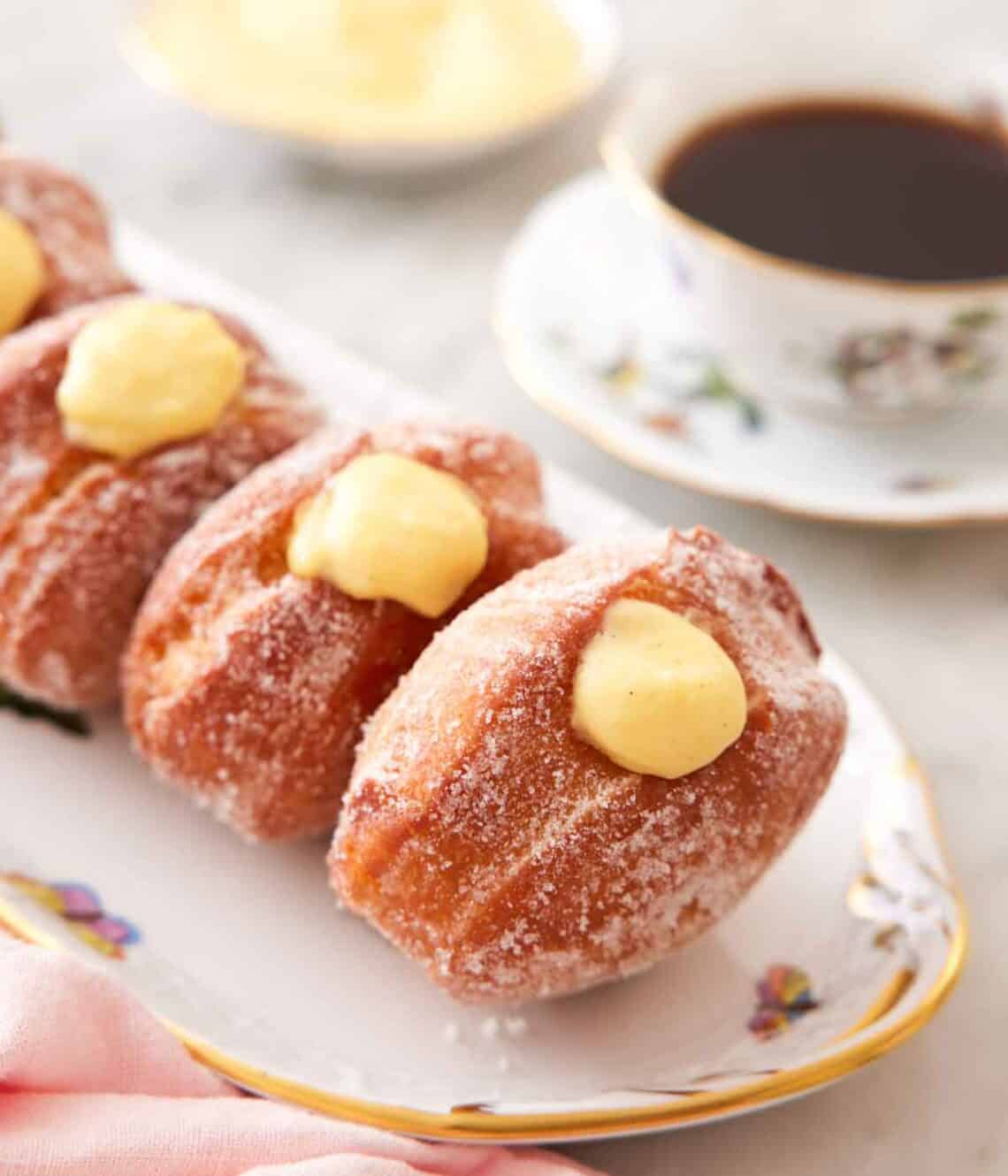 Close up on a platter of bomboloni, Italian donuts, with a cup of coffee in the background.