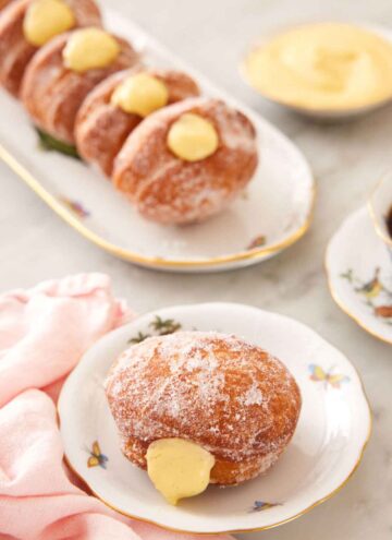 A plate with a bomboloni with a platter with four more in the background.