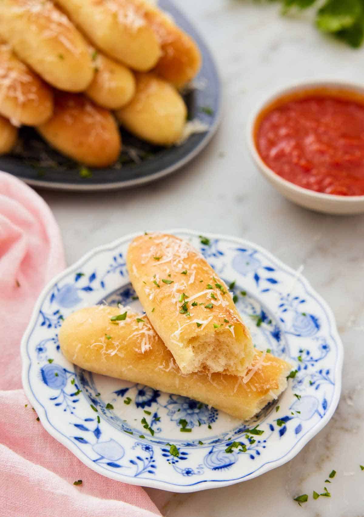 A plate with a breadstick torn in half with sauce and more bread in the background.