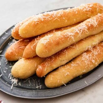 A platter of breadsticks with grated parmesan sprinkled on top.