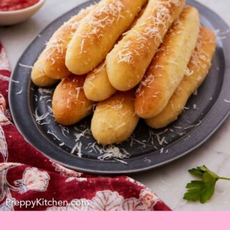Pinterest graphic of a grey platter of breadsticks with parmesan grated on top.