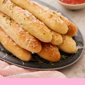 Pinterest graphic of a platter of breadsticks with parmesan grated on top with sauce in the background.