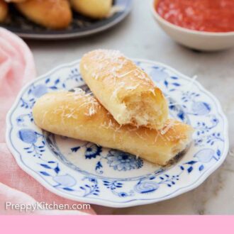 Pinterest graphic of a plate with a breadstick torn in half with one half stacked on top of the other. Sauce and more bread in the back.
